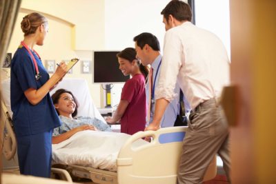 Medical Team Meeting Around Female Patient In Hospital Room